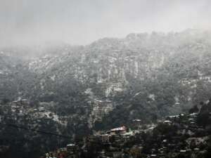 Snow-covered hills and misty clouds over Kasauli, India create a serene winter landscape.